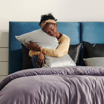 A model in bed hugging the pillow with a light grey pillow case