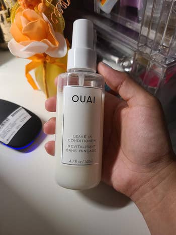 Hand holding OUAI leave-in conditioner bottle