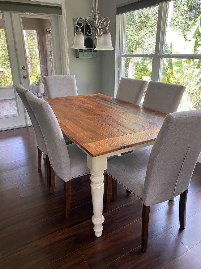 A wood dining table with six grey upholstered chairs in a room with glass doors and a chandelier