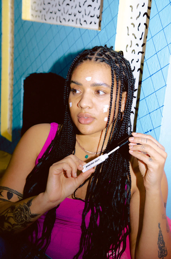 Model holding the spot treatment stick with dots where they applied the treatment on their face