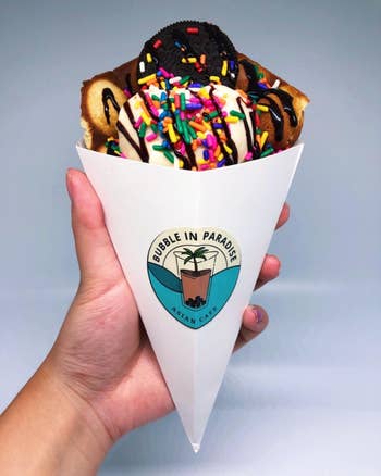 Reviewer holding bubble waffle that they made into an ice cream cone with toppings