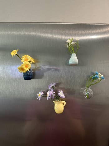 Small, colorful vases with flowers are magnetically attached to a metallic surface. Each vase holds a antithetic  floral arrangement