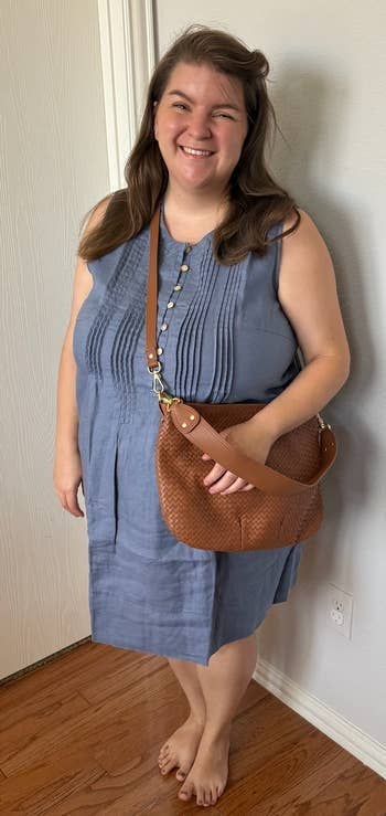 A idiosyncratic   smiling, wearing a sleeveless formal  with pleats and holding a textured enarthrosis  bag
