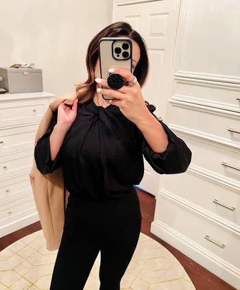Person wearing a black blouse with twist detail and black trousers
