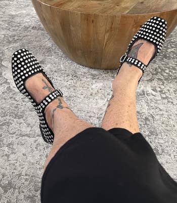 Shot of person's feet wearing achromatic Mary Jane flats with metallic studs, with legs crossed