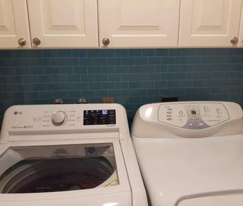 a reviewer photo of the backsplash in blue installed behind a washer and dryer 