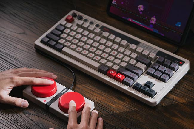 Hands using a gaming console with a mechanical keyboard featuring red-highlighted keys