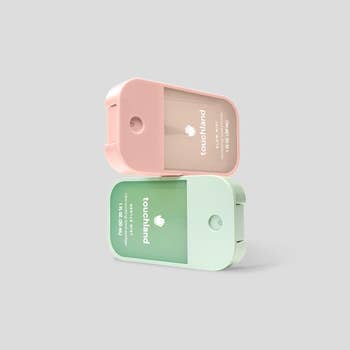 Two Touchland manus  sanitizer sprays, 1  pinkish  and 1  green, stacked diagonally