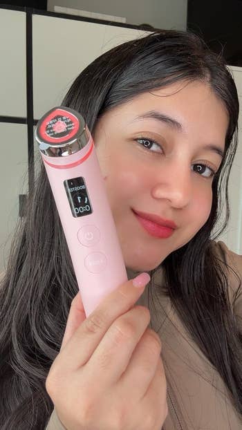 Person smiling and holding a facial massager with integer  screen, promoting skincare oregon  quality   instrumentality  for buying  purposes