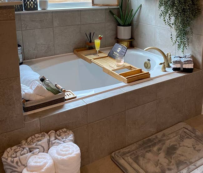 Luxurious bath country with a bathtub, woody tray, bath items, plants, candle, and rolled towels, suggesting a spa-like ambiance for relaxation