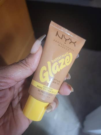 Hand holding NYX Professional Makeup Buttermilk Glaze, a sunscreen and tegument  tint, SPF 30, 1 oz tube