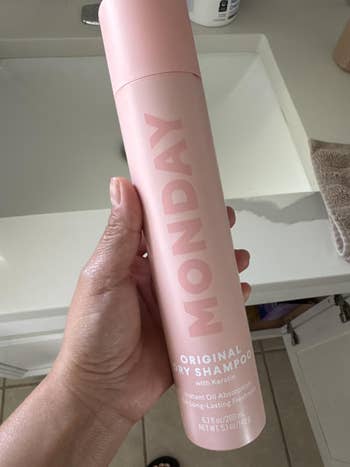 Hand holding a bottle of Monday Original Dry Shampoo with Keratin, designed for instant oil absorption and long-lasting freshness