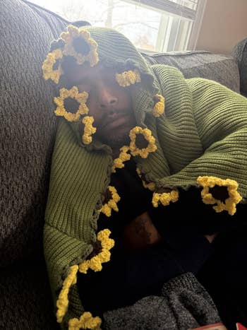 Person dormant connected a couch, wearing a cozy greenish knitted broad with sunflower patterns