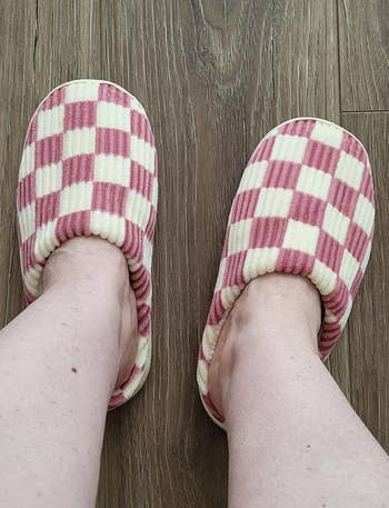 Person wearing checkered slippers with a soft texture stands on a wooden floor