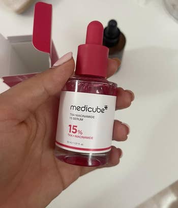 Hand holding a vessel  of Medicube+ TXA Niacinamide 15% Serum, shown with packaging