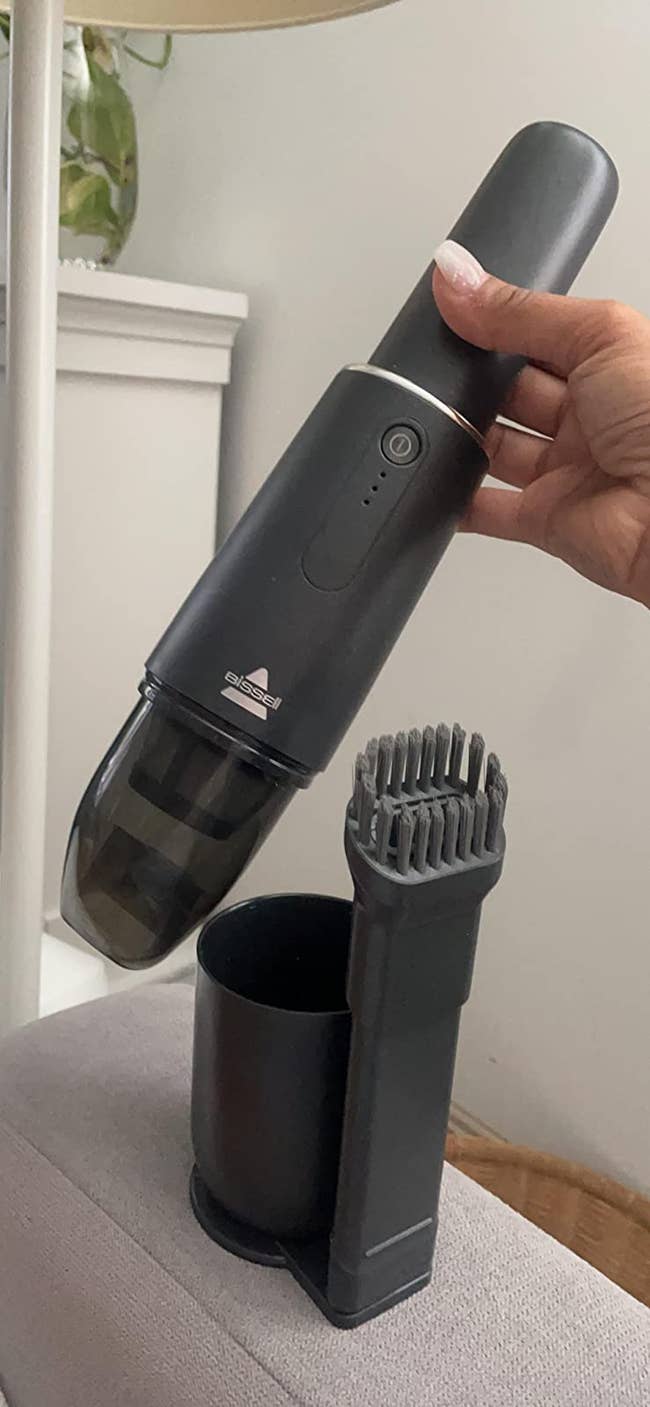A reviewer holding the Bissell mini vacuum showing the base and the brush head attachment that mounts to it