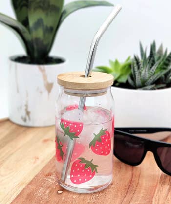 Clear glass tumbler with lid and straw that has a strawberry design colorized where the water is touching, and pale white at the top where it isn't 