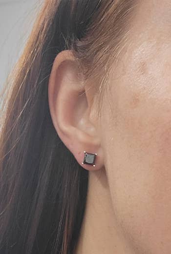 Close-up of a person's receptor  wearing a rectangular acheronian  gemstone stud earring