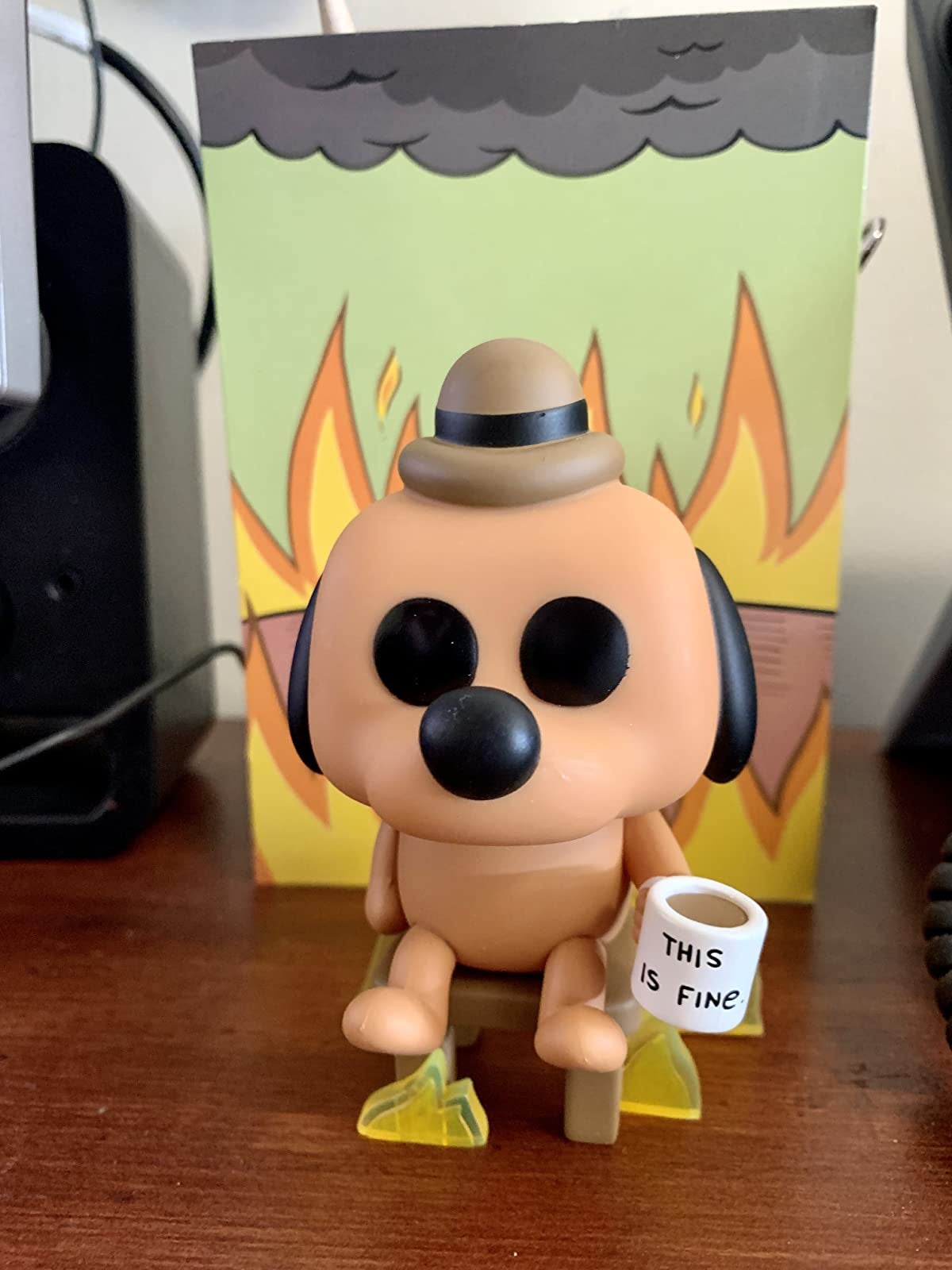 figure of dog in chair with this is fine much with little plastic flames at the base, on a reviewer's desk with flame and smoke background
