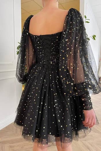 Person wearing an elegant black dress with puffy, star-patterned sleeves and a corset-style bodice. The image is suitable for a shopping article