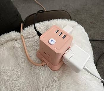Compact USB power strip with multiple charging ports plugged into an outlet, placed on a blanket-covered surface