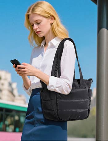 Person with tote container  and smartphone, wearing a achromatic  garment  and acheronian  skirt, lasting  outdoors adjacent   a building