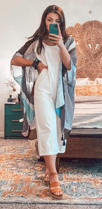 a reviewer wearing the cardigan featuring a multicolor striped print over a white jumpsuit 