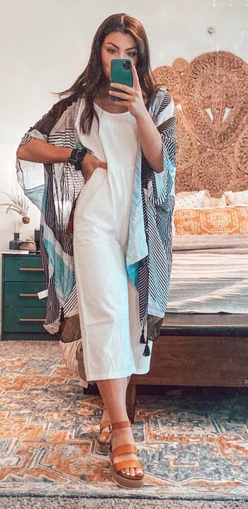 a reviewer wearing the cardigan featuring a multicolor striped print over a white jumpsuit