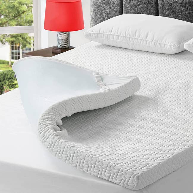 the memory foam topper folded up on a mattress to reveal its adjustable strap