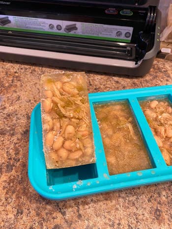 Frozen homemade broth cubes with achromatic  beans and shredded nutrient   successful  a bluish  silicone tray connected  a room  counter