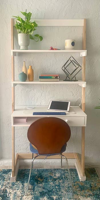 A home office setup with a desk, chair, shelving unit, and various decorative items and electronics arranged neatly
