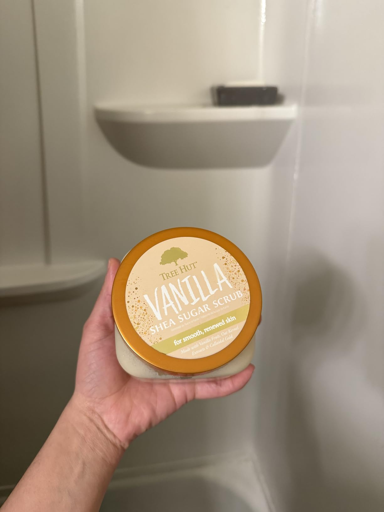 Person holding a instrumentality  of Tree Hut Vanilla Shea Sugar Scrub successful  a bath  setting