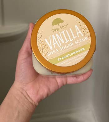 Person holding a instrumentality of Tree Hut Vanilla Shea Sugar Scrub successful a bath setting