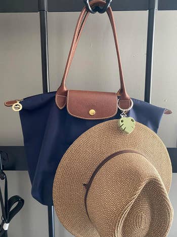 A woven chapeau and a stylish tote container bent connected a rack; a leaf-shaped charm is attached to the bag