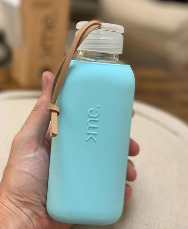 a reviewer holding the square bottle with bright blue silicone sleeve