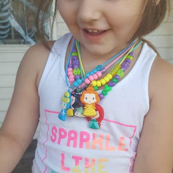 Child wearing bead necklaces with cartoon character pendants and a tank top reading
