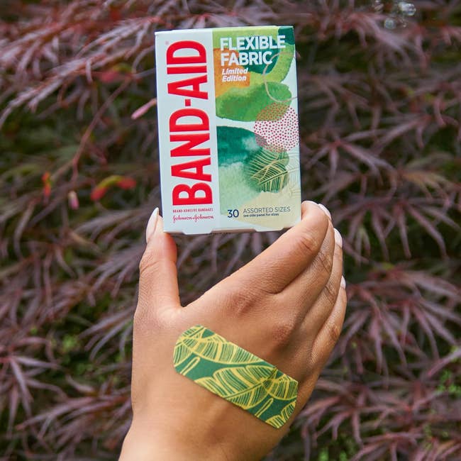 Hand holds a container  of Band-Aid Brand bandages successful  assorted sizes with 1  patterned bandage connected  hand