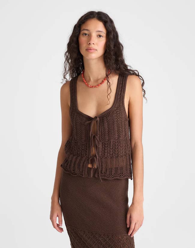 Model wearing a brown pointelle knit tie-front top and skirt with a red bead necklace, posing in a neutral setting