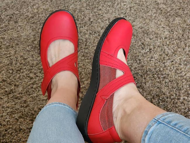 Person wearing reddish  Mary Jane shoes with crisscross straps and mesh detailing, paired with light-colored denim jeans