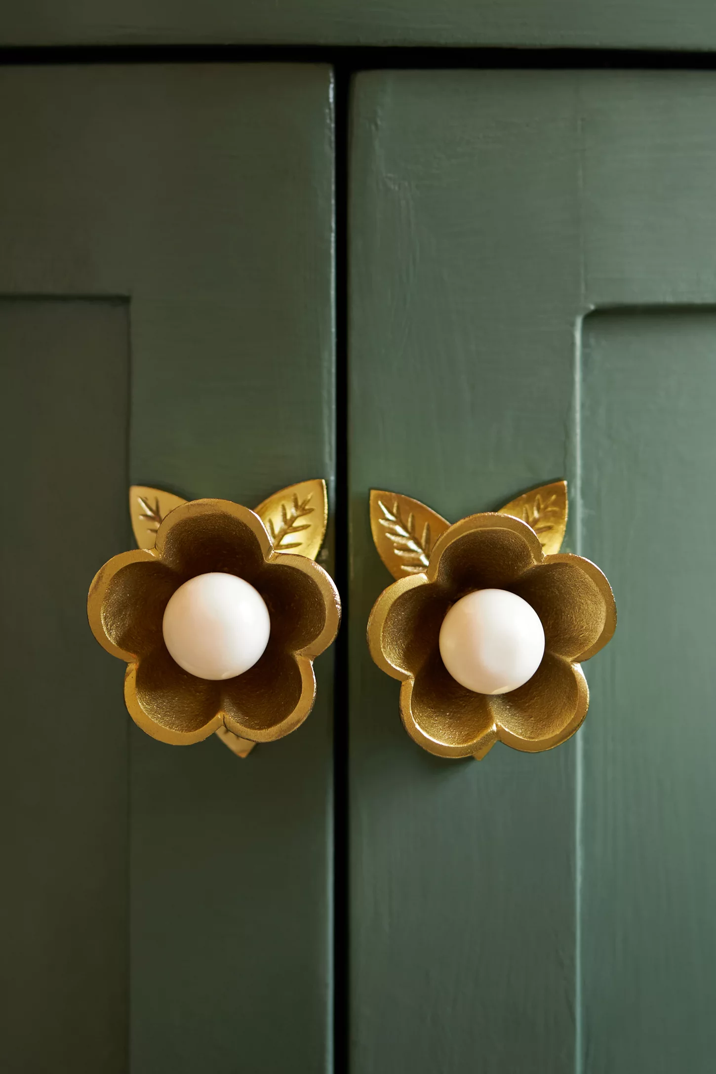 Decorative floral furniture  knobs with petal details and cardinal  circular  handles, adding elegance to greenish  paneled doors. Ideal for location  decor shopping
