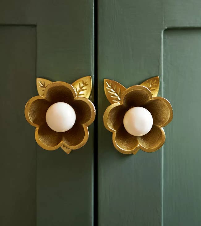 Decorative floral furniture knobs with petal details and cardinal circular handles, adding elegance to greenish paneled doors. Ideal for location decor shopping