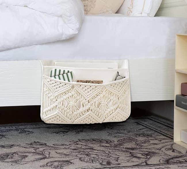 ivory macrame caddy inserted between bed frame and mattress holding remotes, glasses, etc.