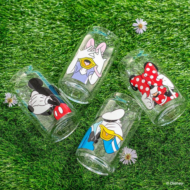 Four Disney character-themed drinking glasses on grass