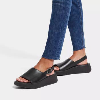 Person wearing black platform sandals and cropped jeans, focused on footwear for shopping context