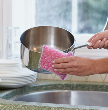 hands using the sparkly pink sponge to scrub a pot