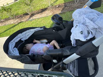 A babe  sleeps successful  a stroller outdoors, covered with a partially disposable   blanket, adjacent   a grassy country  and a metallic  table