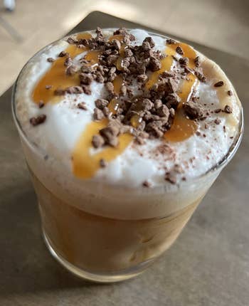 Glass of iced java topped with frothy cream, caramel drizzle, and cocoa shavings, sitting connected a table