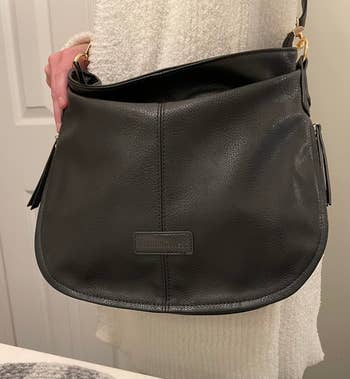 Person holding a leather handbag with a curved design and a designer label on the front, suitable for shopping articles