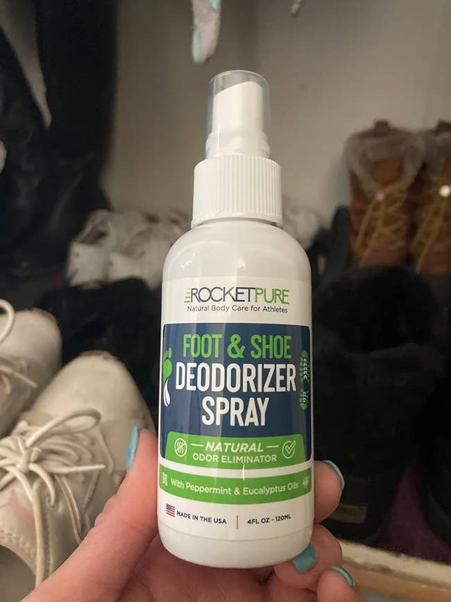 Hand holding a bottle of Rocket Pure foot and shoe deodorizer spray with shoes in the background