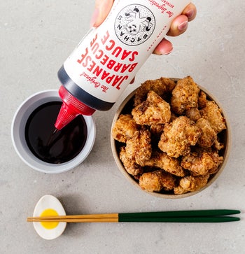 A hand squeezing the sauce into a dipping cup next to a bowl of chicken